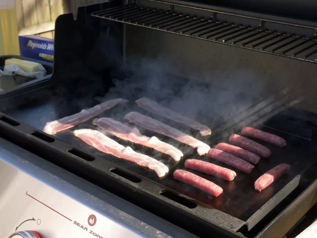 Outdoor brunch cooking on a cast iron griddle with bacon and eggs