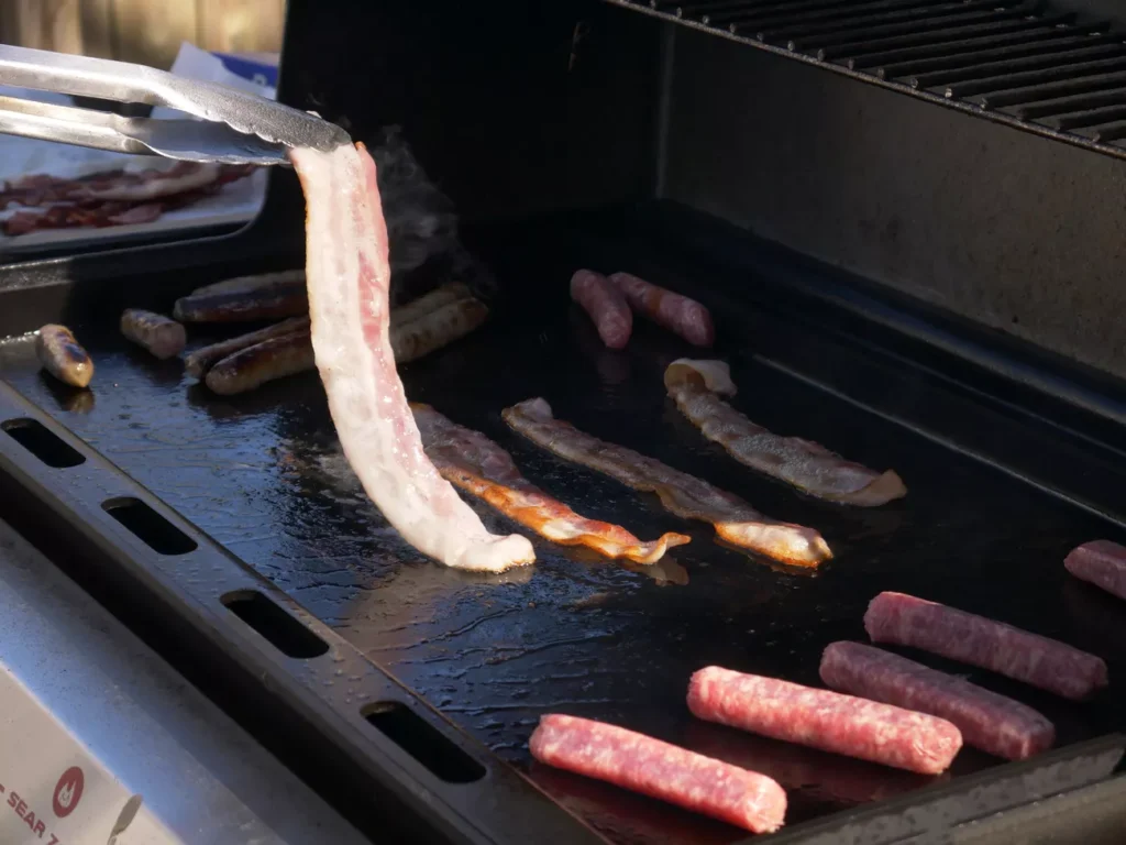 Outdoor brunch cooking on a cast iron griddle with bacon and eggs
