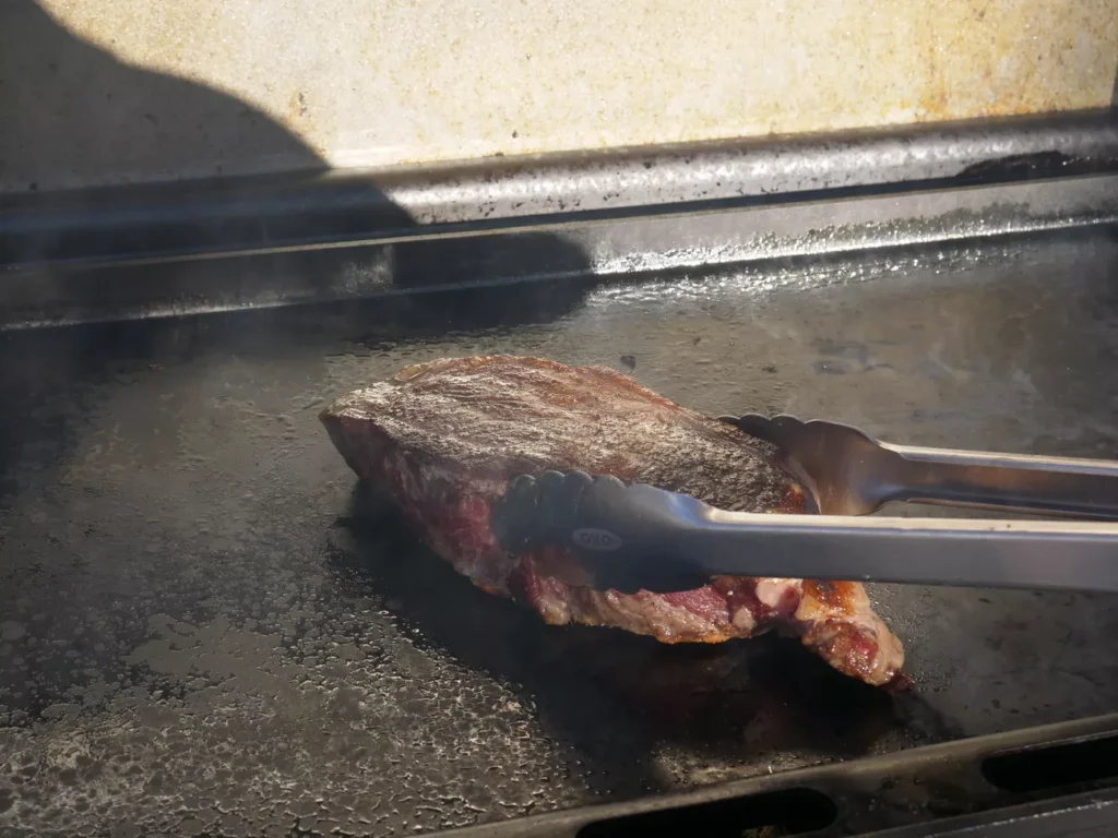 Outdoor brunch cooking on a cast iron griddle with bacon and eggs